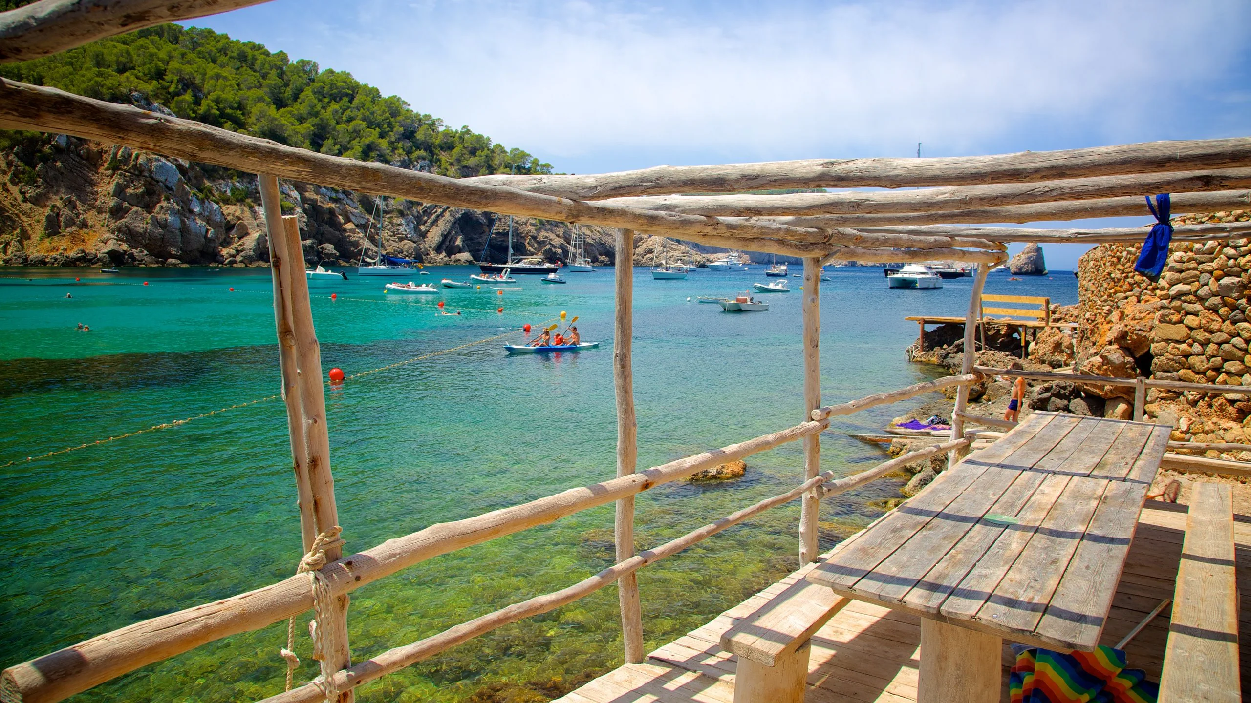 Terrasse en bois face à la crique de Benirràs et ses bateaux au mouillage, Ibiza