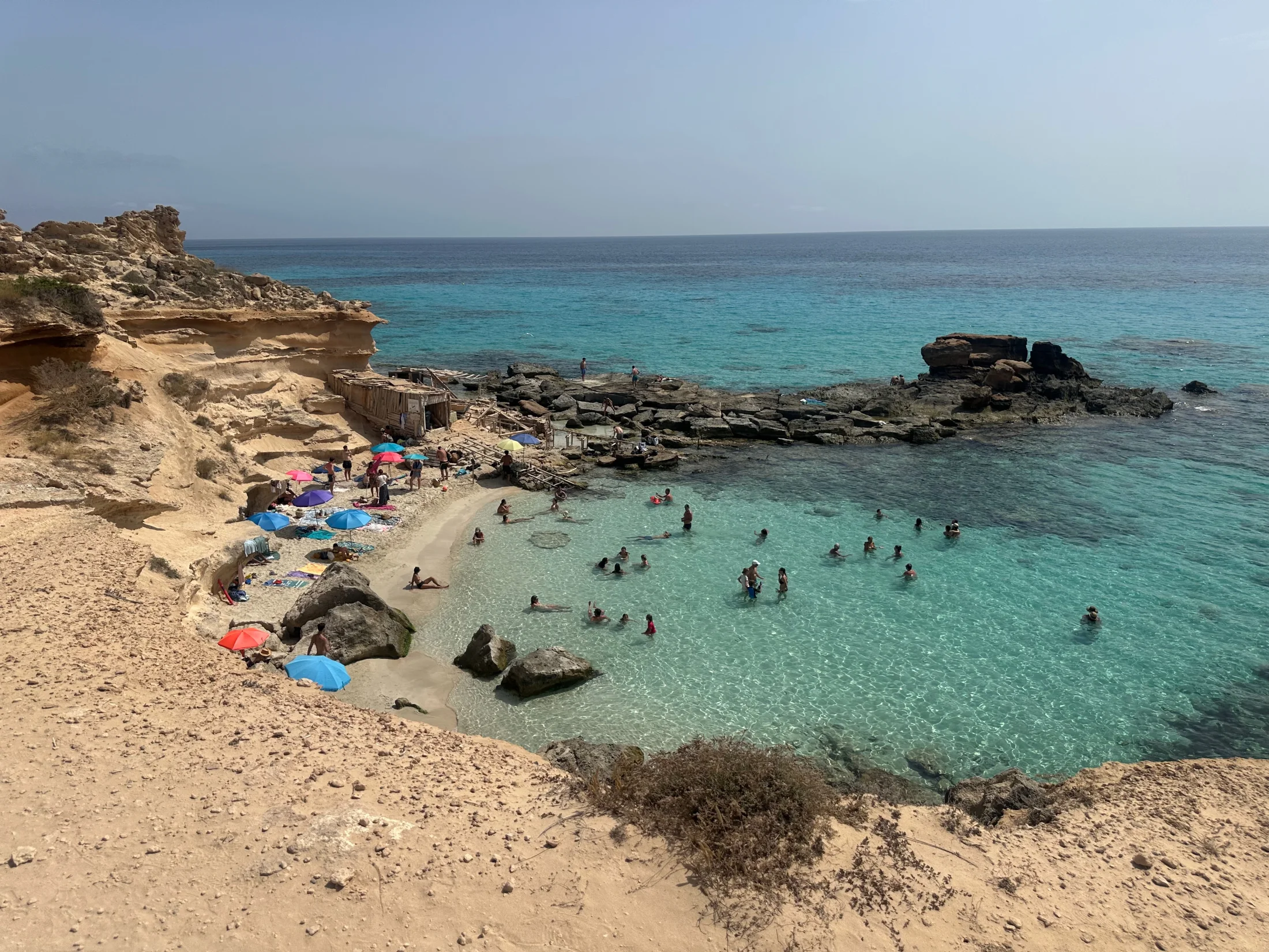Panorama du Caló des Mort à Formentera, sable, parasols et eau turquoise depuis la falaise