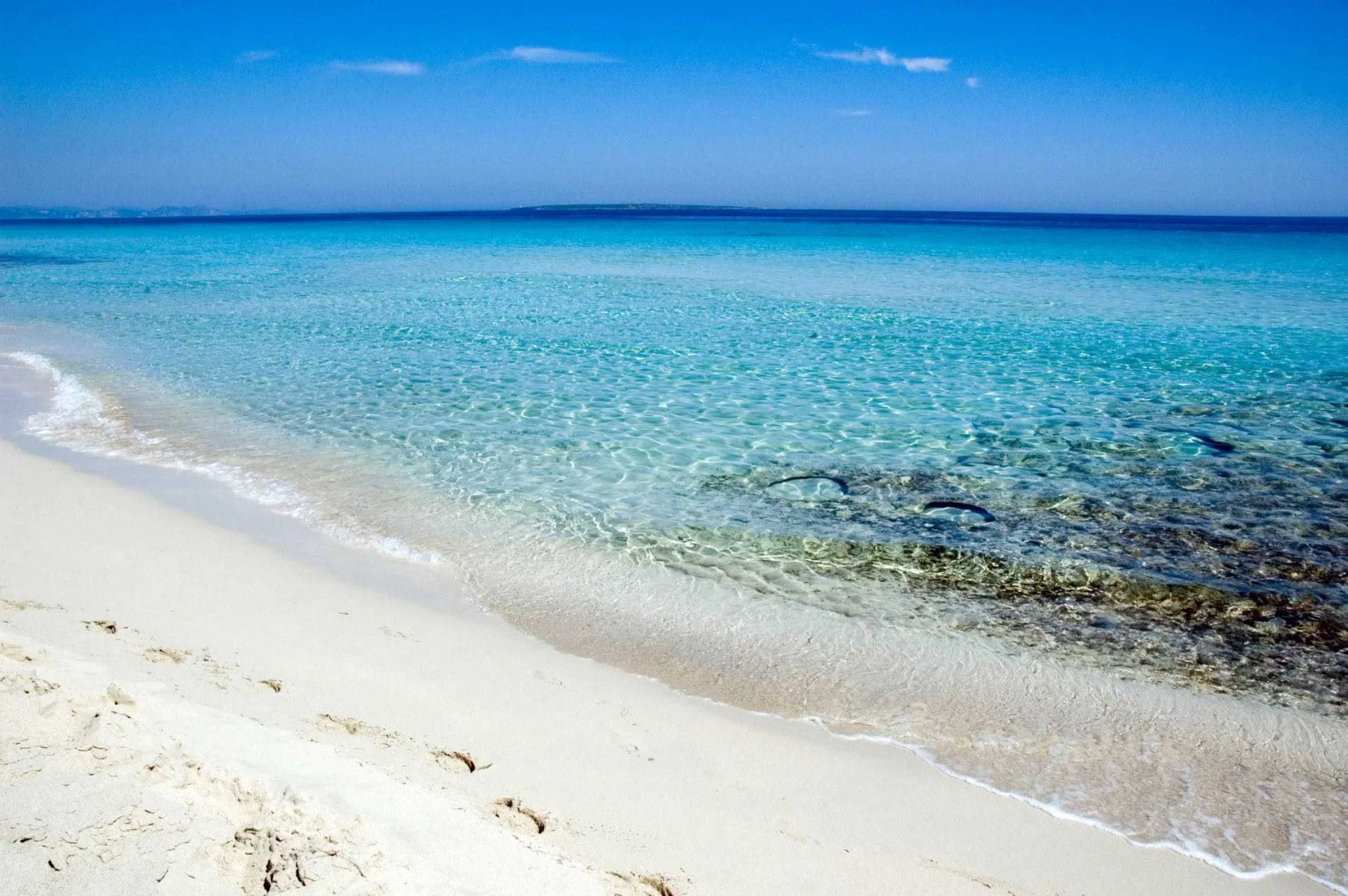 Sable blanc et eau cristalline de Platja de Llevant à Formentera, îlot à l'horizon