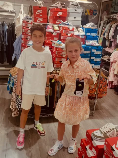 Deux enfants habillés en marques designer devant le rayon chaussures Club ABC
