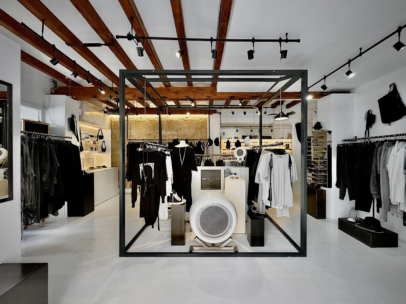 Intérieur de reVOLVER Ibiza, vêtements noirs et blancs sous poutres apparentes