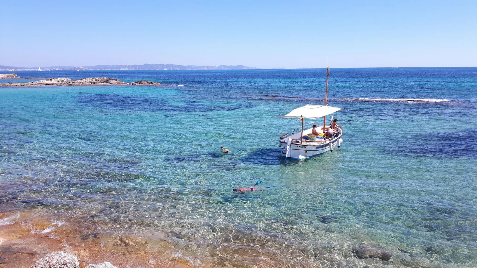 Llaüt traditionnel ancré dans l'eau turquoise, baigneurs en snorkeling autour