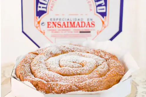Ensaimada en spirale devant sa boîte de pâtisserie